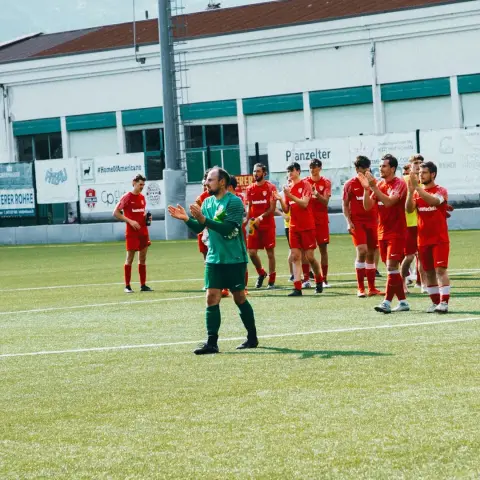 Spieler des AFC Terlan in roten Trikots applaudieren den Zuschauern auf dem Rasen, davor klatscht der Torhüter in Grün nach dem Spiel gegen Bruneck.
