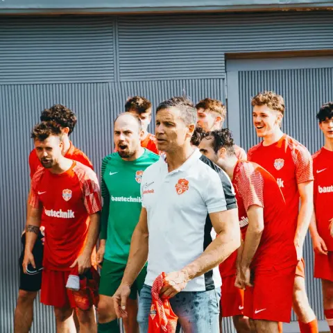 Mannschaft des AFC Terlan in roten Trikots mit bautechnik-Sponsor, im Vordergrund ein Trainer in weißem Poloshirt mit Vereinswappen, der ein rotes Trikot trägt.