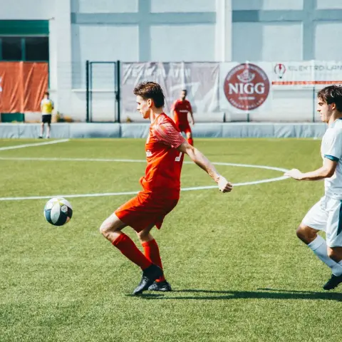 Spielszene: Ein Spieler in roter Trikot führt den Ball am Spielfeldrand, im Hintergrund das Sponsorenbanner von NIGG.