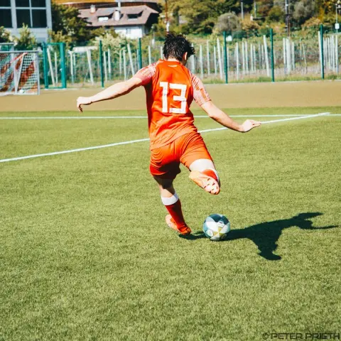 Spieler des AFC Terlan mit Trikotnummer 13 schießt im Spiel gegen Bruneck den Ball auf dem Kunstrasen.