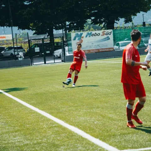 Spielszene: Ein Spieler in roter Trikot führt den Ball am Spielfeldrand, im Hintergrund wirbt die Bande für MeboSüd, ein Gegner ist angeschnitten.