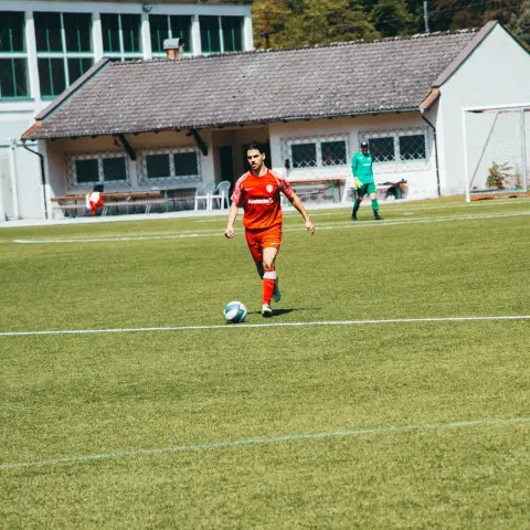 Spieler des AFC Terlan in roter Trikot führt den Ball auf dem Rasenplatz, im Hintergrund steht der Torwart in Grün am Tor.