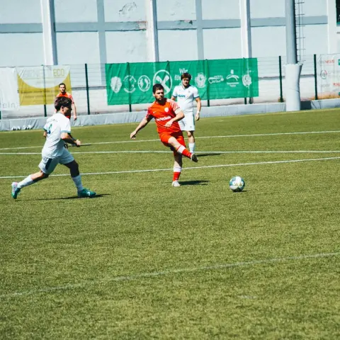 Spielszene: Ein Spieler in Orange schießt den Ball, Gegner in Weiß laufen mit beim Spiel Terlan gegen Bruneck.
