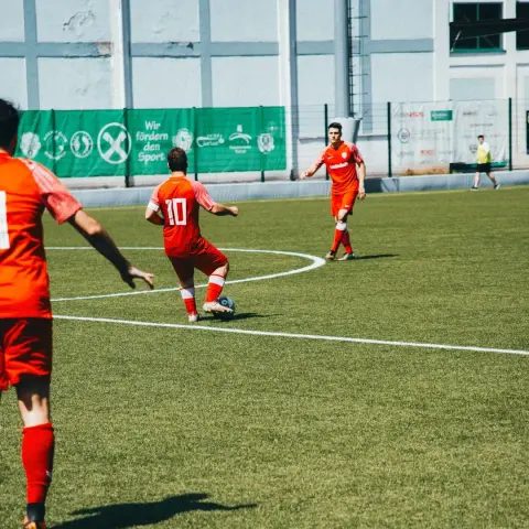 Spielszene: Ein Spieler in oranger Trikotnummer 10 führt den Ball am Mittelkreis, ein Mitspieler läuft im Hintergrund mit, im Bild ist das Spiel des AFC Terlan gegen Bruneck.