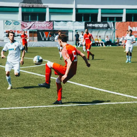 Spielszene: Ein Spieler in Orange schießt den Ball, während ein Gegenspieler in Weiß zusieht, im Spiel AFC Terlan gegen Bruneck.