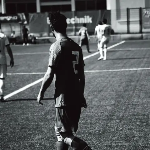 Schwarz-weiß-Spielszene: Ein Spieler mit der Nummer 2 geht über den Kunstrasen, im Hintergrund Mitspieler und die Bande mit dem Sponsor Bautechnik.