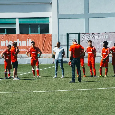 Spieler des AFC Terlan in roten Trikots stehen auf dem Kunstrasen und hören einem Trainer zu, im Hintergrund eine Bande mit Sponsorenwerbung.